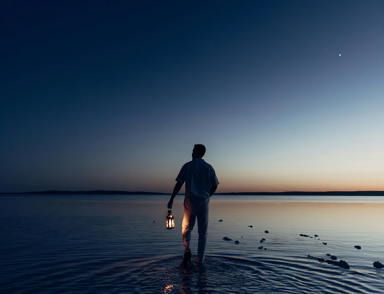 Personne observant l'horizon avec une lanterne, symbole de recherche de sens et de clarté